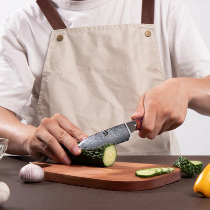 Chef utilisant couteau utilitaire Wildmok Damascus manche résine rouge – découpe concombre sur planche bois