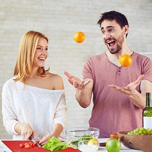 Couple joyeux en cuisine utilisant planche à découper plastique rouge flexible pour couper légumes