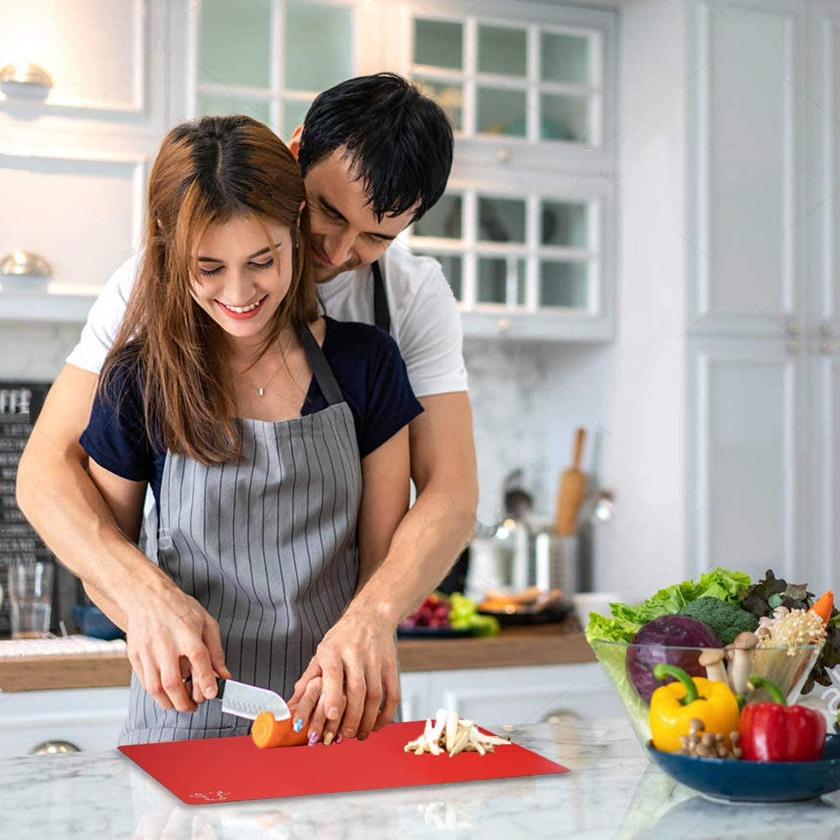 Couple cuisinant ensemble avec planche à découper plastique rouge flexible sur plan de travail marbre
